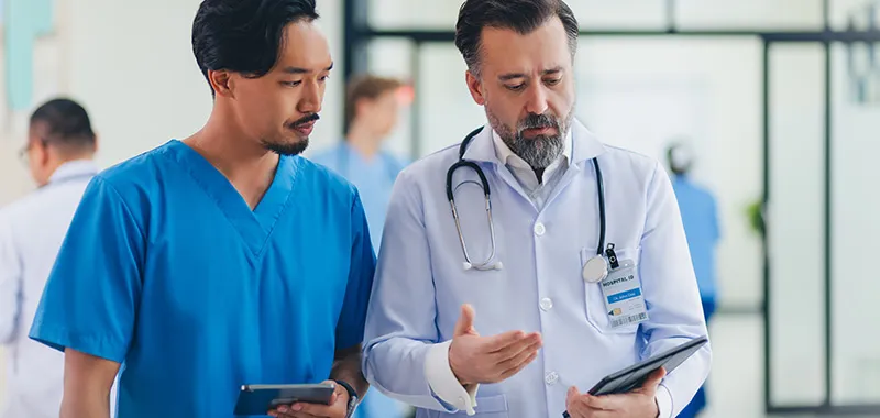 Male doctor and male nurse discussing infection control looking at tablet computer 