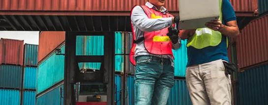 Workers looking at a laptop surrounded by containers